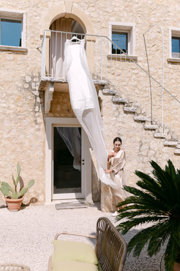Preparazione della sposa a Villa Mosconi Bertani con abito da sposa appeso e damigella nel cortile