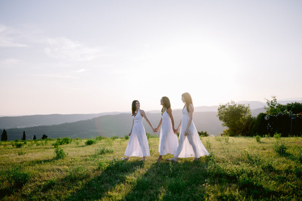 mamma e figlie in abiti chiari che camminano insieme al tramonto in un servizio fotografico all’aperto a Verona