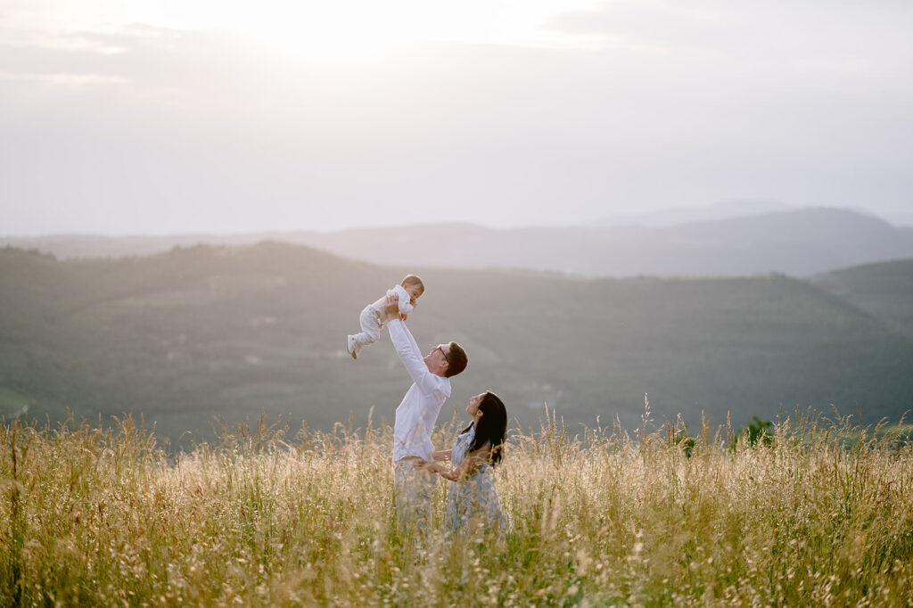 Padre che solleva il figlio in aria mentre la madre osserva durante un servizio fotografico di famiglia al tramonto a Verona
