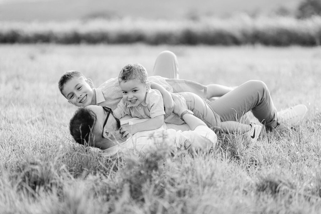 adre che gioca con i figli sdraiati sull’erba durante un servizio fotografico di famiglia a Verona
