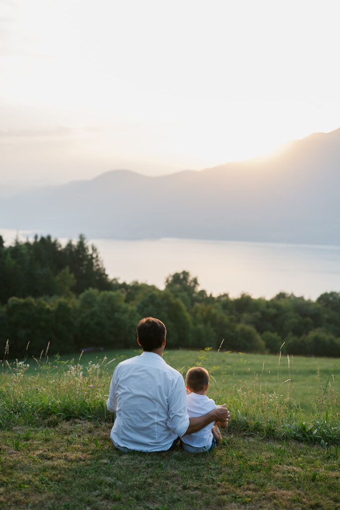 Padre e figlio seduti di spalle con vista sul lago al tramonto durante un servizio fotografico di famiglia