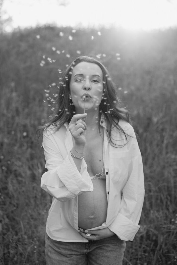 Donna in gravidanza che soffia su un soffione in un campo durante un servizio fotografico di maternità a Verona