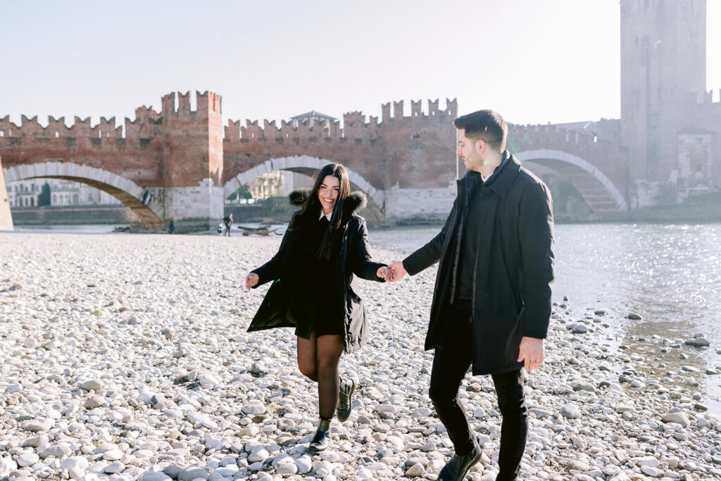 Verona proposal photographer capturing a couple walking by Ponte Pietra and the Adige river
